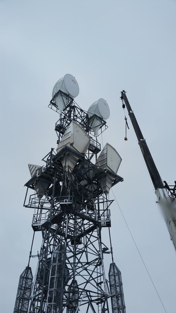 Crane rigged to a self-support tower carrying microwave horns and drum dishes