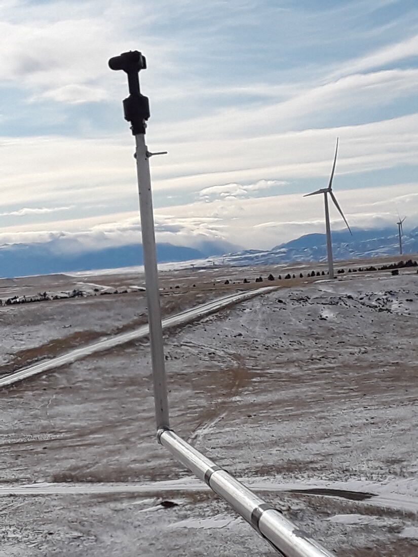 Survey prism and rod set on a snow-dusted site with wind turbines beyond