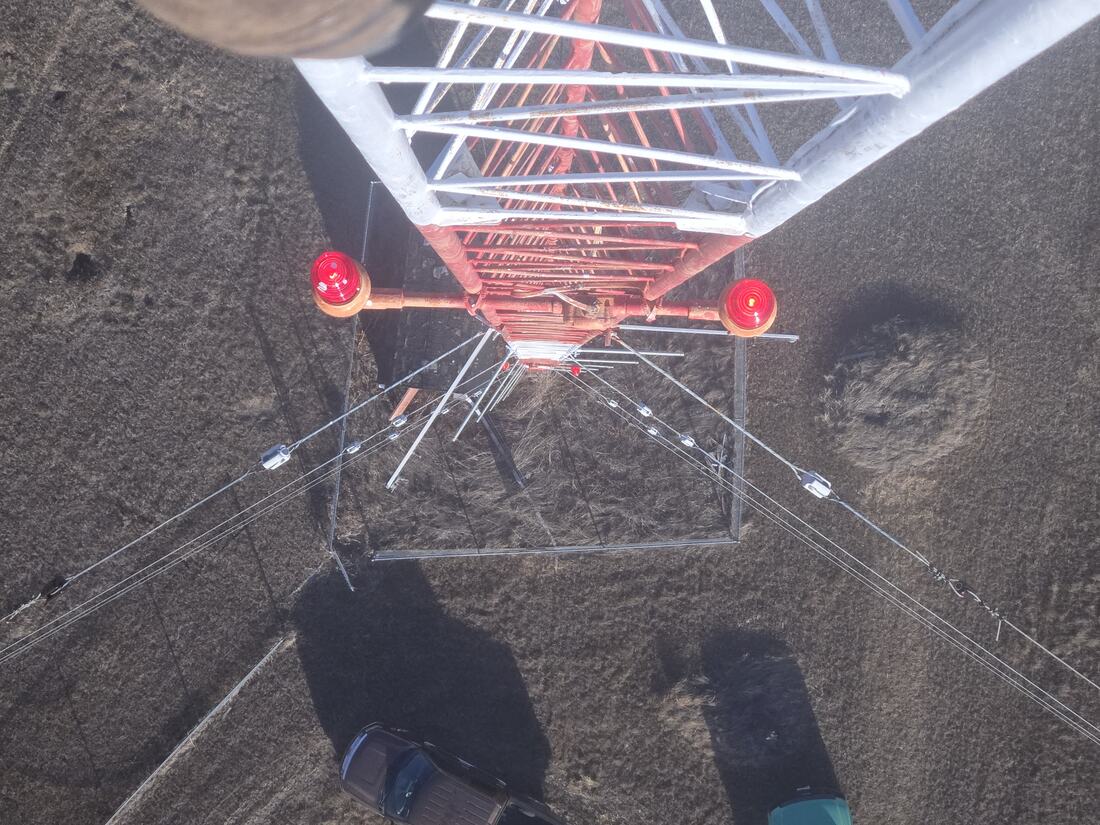Looking straight down a guyed tower past the obstruction beacons to the compound